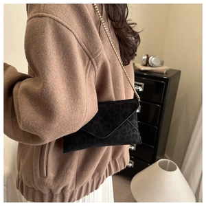 Close-up of leopard print envelope bag with gold chain strap on a model in home setting