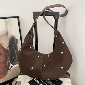 Borsa hobo a mezzaluna in camoscio marrone con borchie dorate su una valigia