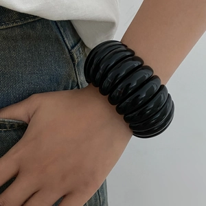 Detail of wide black chunky resin bracelet styled with casual white shirt and denim