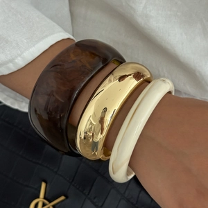 Primo piano di tre bracciali sovrapposti in oro, tartaruga e resina marmorizzata