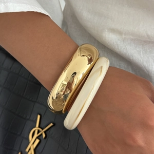 Dettaglio di un bracciale rigido dorato e uno in resina marmorizzata con borsa nera