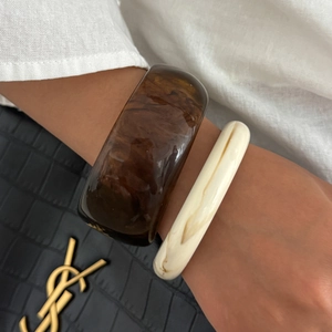Dettaglio di bracciali sovrapposti in resina tartarugata e marmo crema sul polso