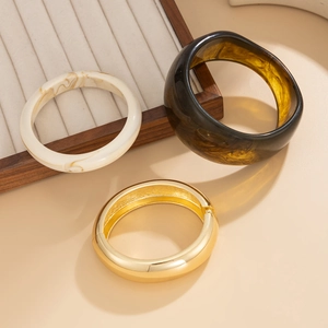 Dettaglio di bracciale rigido in metallo dorato con bracciali in resina e marmo