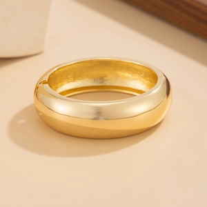 Dettaglio del bracciale rigido dorato largo con finitura a specchio e cerniera a scomparsa