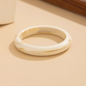 Dettaglio di un bracciale in resina crema effetto marmo su sfondo elegante e minimale