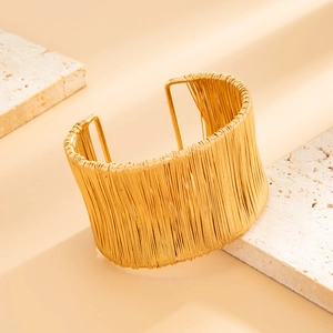 Dettaglio di un ampio bracciale rigido dorato con trama a fili metallici su pietra