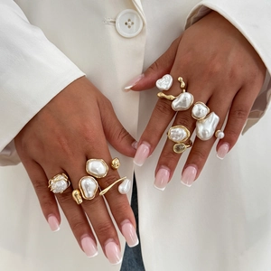 Set di anelli con perle barocche dorate indossati elegantemente su sfondo bianco