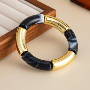 Detalle de la pulsera estilo bambú con tubos de metal dorado y segmentos de acrílico jaspeado