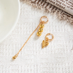 Detail view of asymmetric gold heart earrings with beads and chain on white texture
