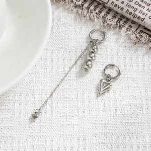 Detail of asymmetric silver heart pendant earrings with sleek chain fringe and metallic beads