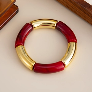 Detalle de pulsera elástica de resina jaspeada roja y metal dorado sobre fondo marfil