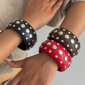 Détail de bracelets punk larges à clous argentés en noir, marron et rouge foncé