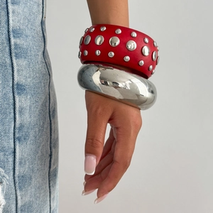 Gros plan sur manchette rouge cloutée et bracelet argenté style punk au poignet