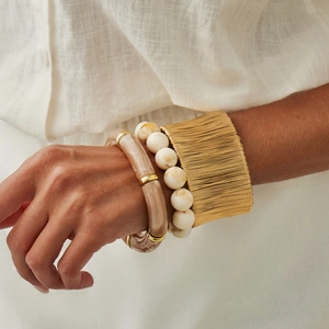Dettaglio di bracciali a strati in resina marmorizzata e metallo dorato intrecciato