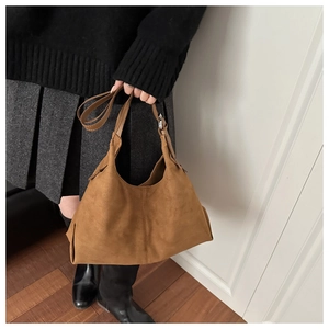Close-up of a brown suede shoulder tote bag with decorative stitching on a female model