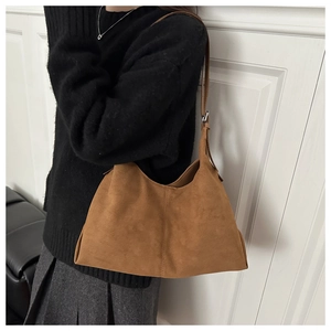 Detail einer braunen Wildleder-Hobo-Tasche mit verstellbarem Gurt an einem Model in Strickmode