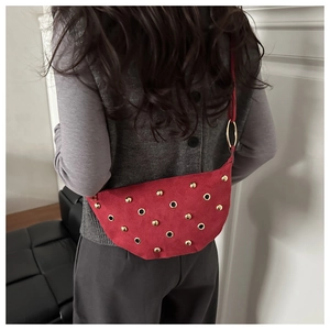 Detail of red suede shoulder bag with gold studs and grommets worn by model
