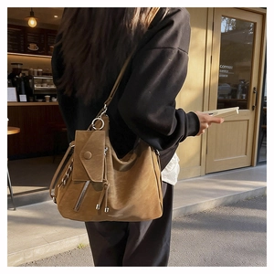 Detail of a brown suede bucket bag with side zippers and a matching mini pouch charm