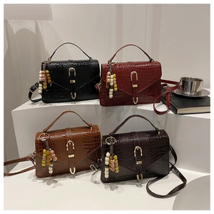Close-up of crocodile pattern handbags in black, burgundy, and brown with beaded tassel