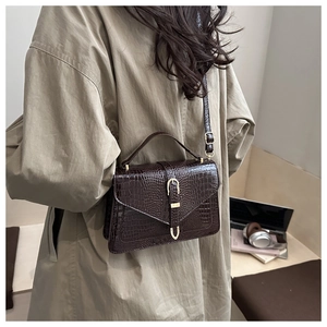 Detail of dark brown crocodile-embossed square bag with gold U-buckle on beige trench coat