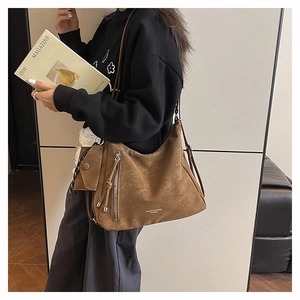Gros plan du sac hobo en daim marron avec pompon décoratif et mini pochette suspendue