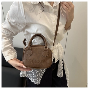 Detail of vintage brown leather shell bag with embossed letters and adjustable shoulder strap