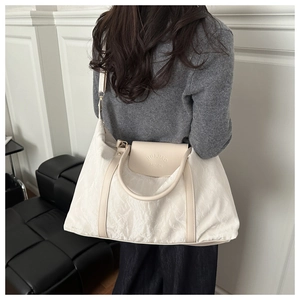 Detail of ivory pleated tote bag showing the embossed brand logo and textured fabric finish