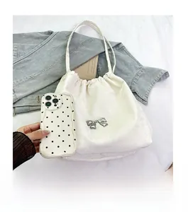 Dettaglio della borsa tote in raso bianco con fiocco metallico accanto a un telefono cellulare