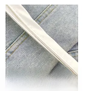 Dettaglio della tracolla in pelle bianca su una borsa tote in denim azzurro chiaro