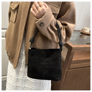 Detail of black suede bucket bag with knotted strap and fashion and classic text