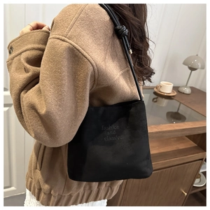 Detail view of black suede bucket bag with embossed text and decorative knotted strap