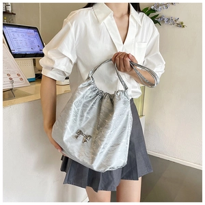 Dettaglio borsa tote argento metallizzato con fiocco e coulisse indossata a spalla