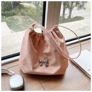 Dettaglio della borsa a secchiello rosa con coulisse e fiocco in metallo argento su legno