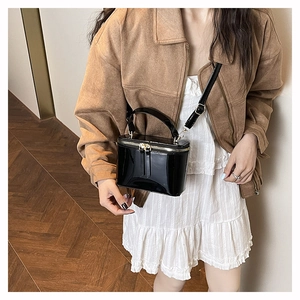 Crossbody box bag in black patent leather with gold zipper shown on a model outfit