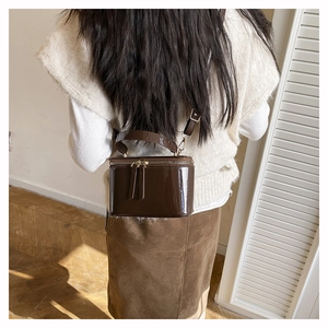 Detail view of dark brown patent leather box bag with gold double zipper and handle