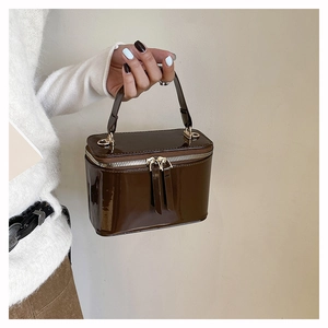 Detail of a deep brown shiny patent leather box bag with gold zippers and handle