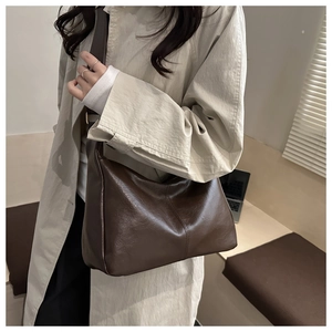 Detail of a vintage dark brown faux leather shoulder bag worn with a beige trench coat