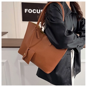 Detail of a large brown faux leather tote bag with a matching wristlet pouch on model