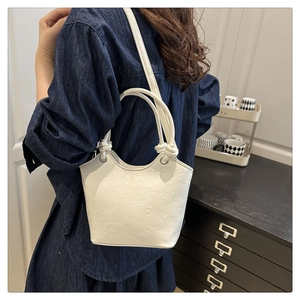 Detail of white bucket bag featuring embossed patterns and a unique cylinder handle
