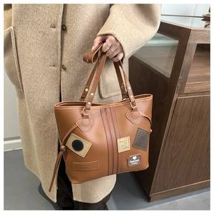 Close-up of brown leather tote bag with vintage patchwork labels and side drawstring details