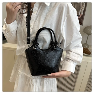 Detail of black embossed PU bucket bag with heart and rabbit patterns on a white dress