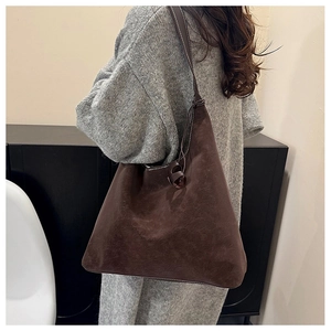 Detail of deep brown suede tote bag with stylish knot strap on a shoulder-worn model