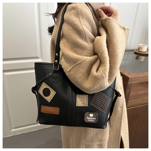 Detail of black leather tote bag with fashion patches worn on a beige wool coat