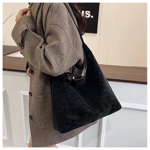 Close-up of black suede tote bag with slim shoulder strap worn with a plaid blazer