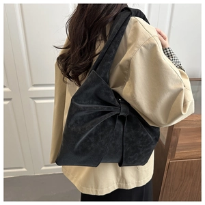 Matte black oversized bow tote bag worn by a model in a minimalist indoor setting