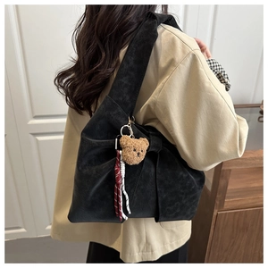 Detail of black suede tote bag with brown bear pendant and wide shoulder strap