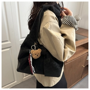 Détail d'un sac cabas noir en daim avec grand nœud et accessoire de petit ours en peluche