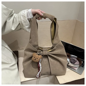 Detail of light brown tote bag with oversized bow design and cute plush bear charm