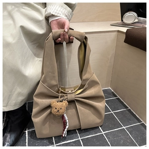 Detail of a large khaki tote bag with bow design and a plush bear pendant on stairs