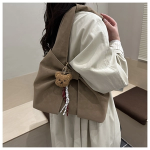 Detail of a brown crescent tote bag with side knot decor and a teddy bear charm